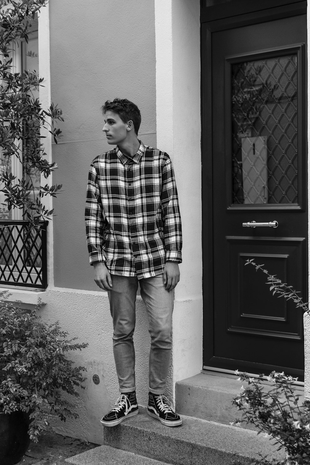 man in plaid dress shirt and blue denim jeans standing beside door