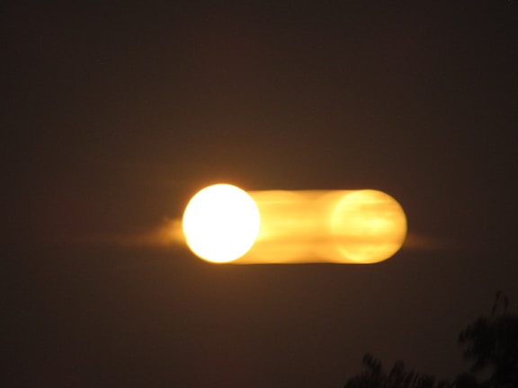 A bright, circular light source appears doubled with motion blur against a dark background, creating a mysterious and dynamic visual effect.