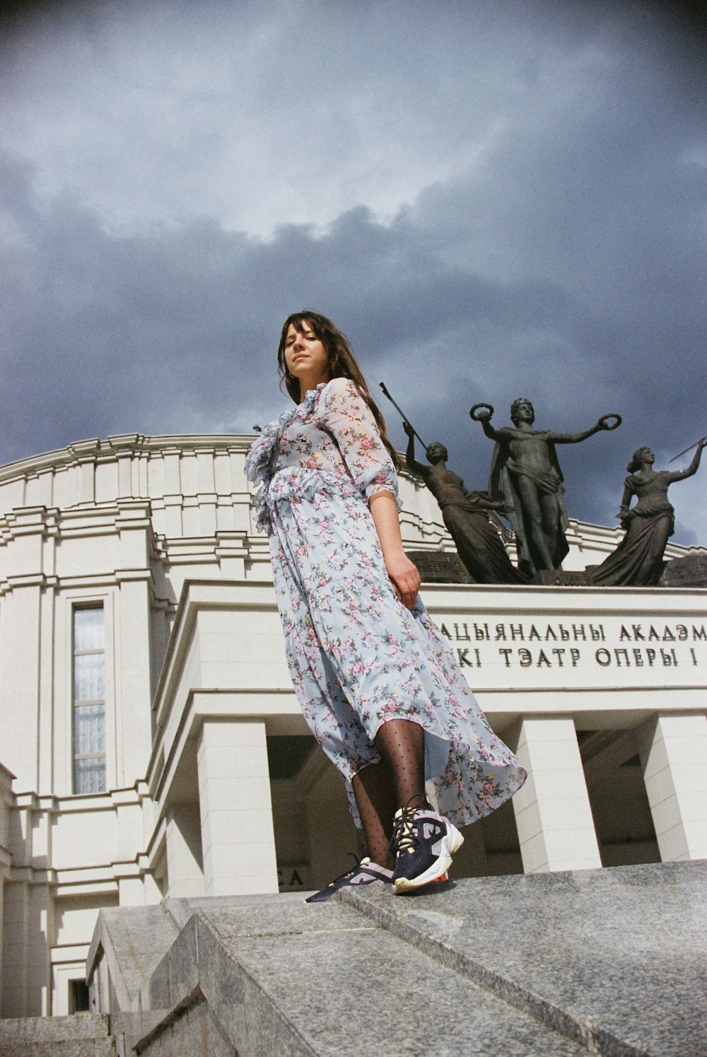 Mujer en vestido floral blanco y azul de pie cerca de la estatua durante el día