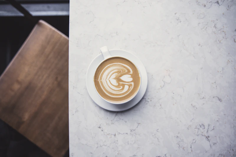 A latte with heart-shaped foam art on a marble café table