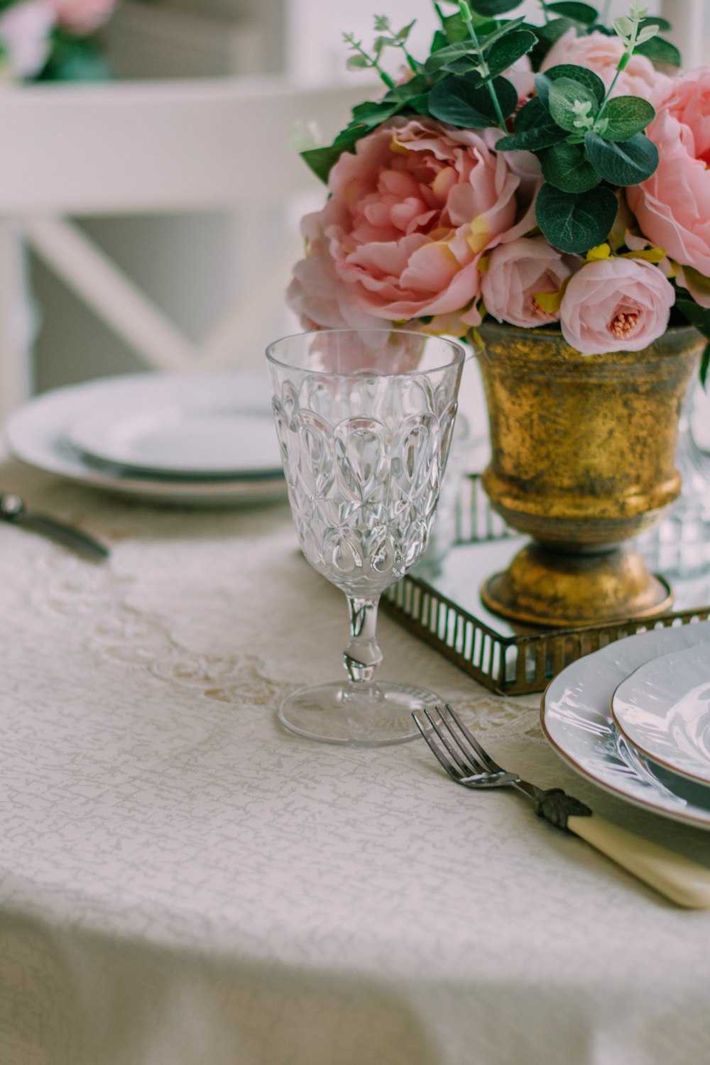 pink roses in clear glass vase beside stainless steel fork and bread knife on white ceramic