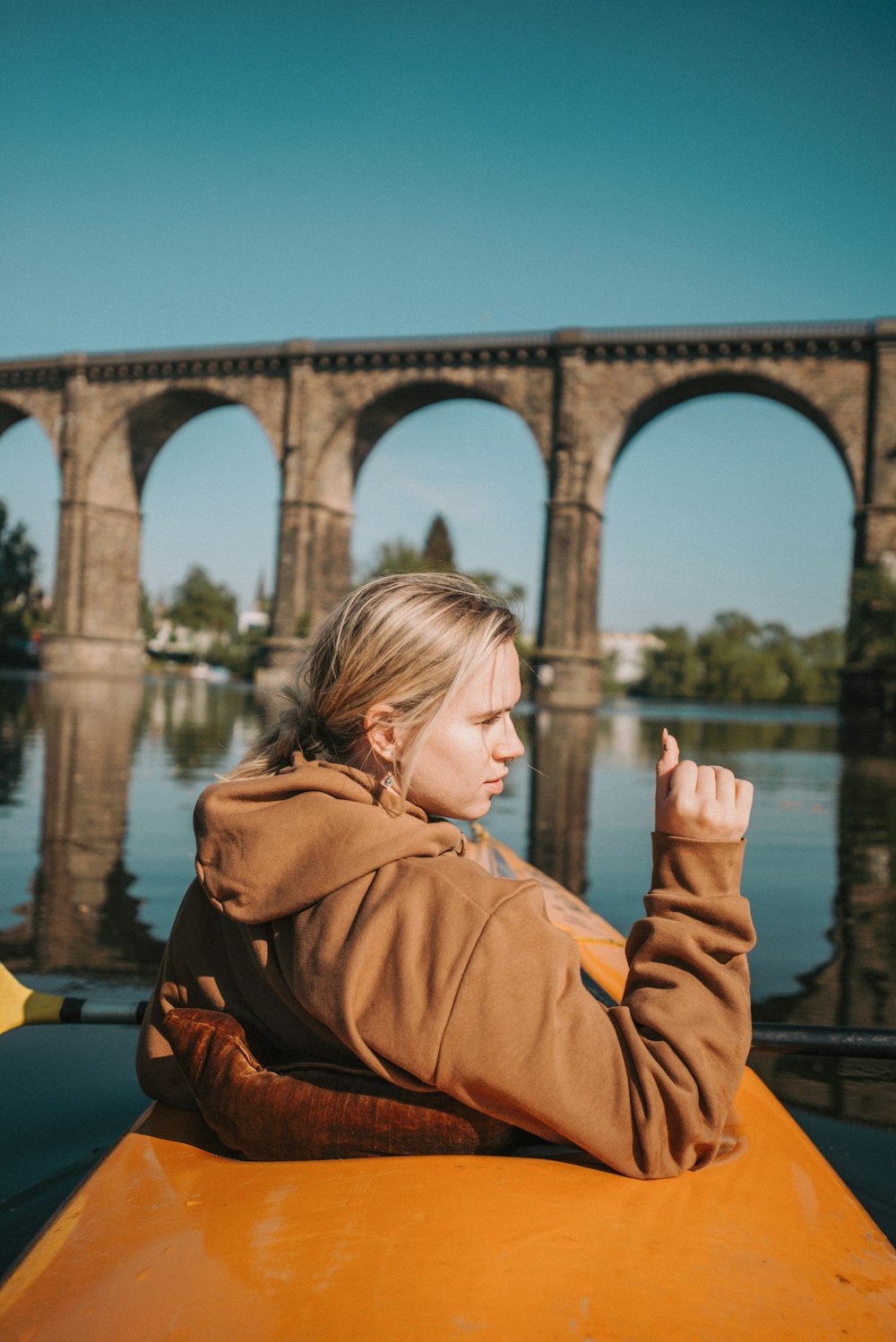 woman in brown hoodie standing near bridge during daytime