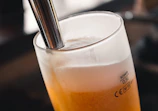 Close-up of hands pouring golden craft beer into a glass with foam.