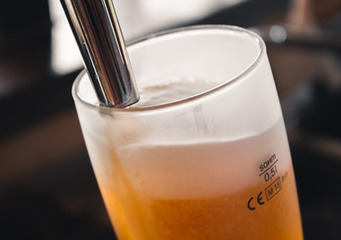 A close-up of a frothy craft beer being poured into a glass at a lively brewery taproom.