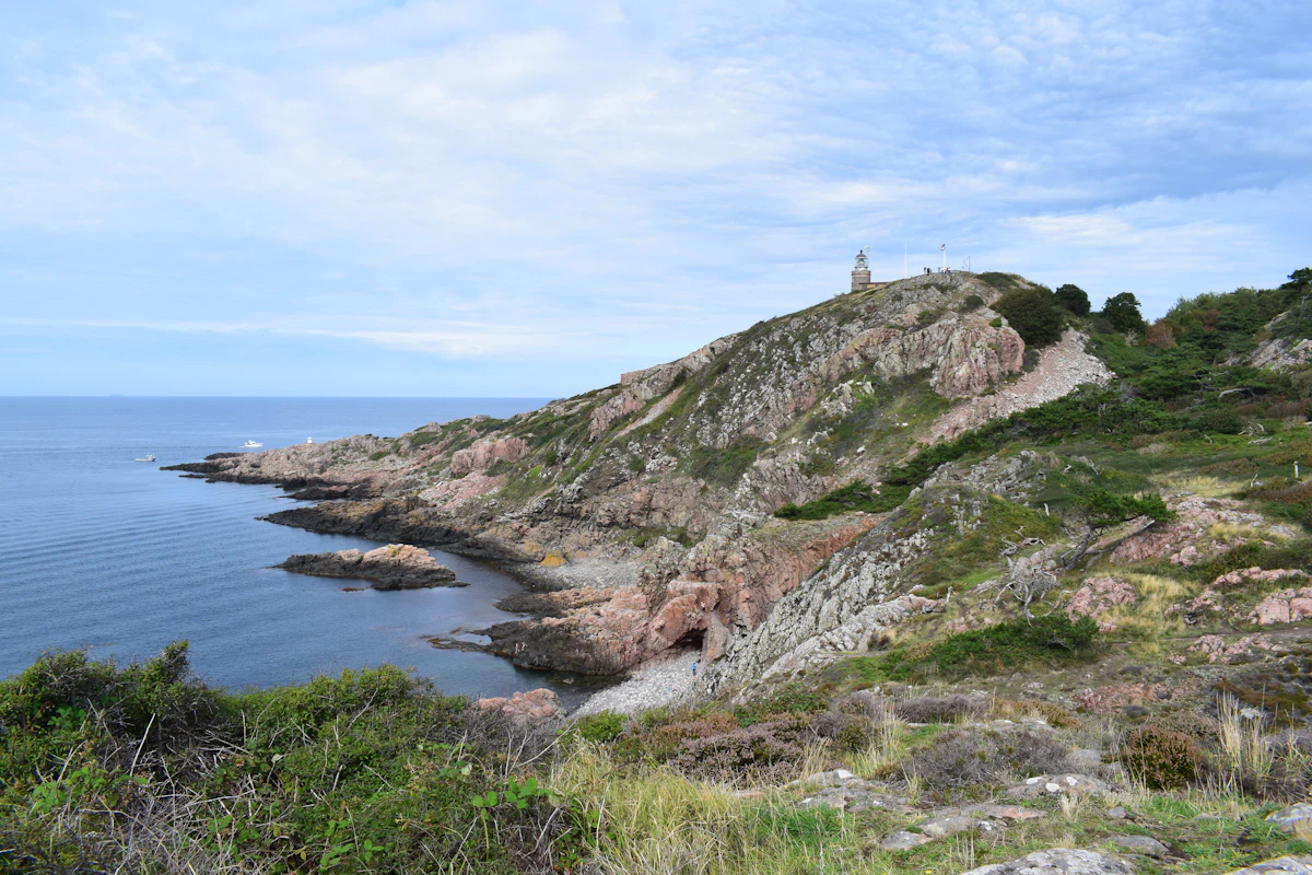 The white lighthouse on the green, rocky tip of Kullaberg, above a calm sea