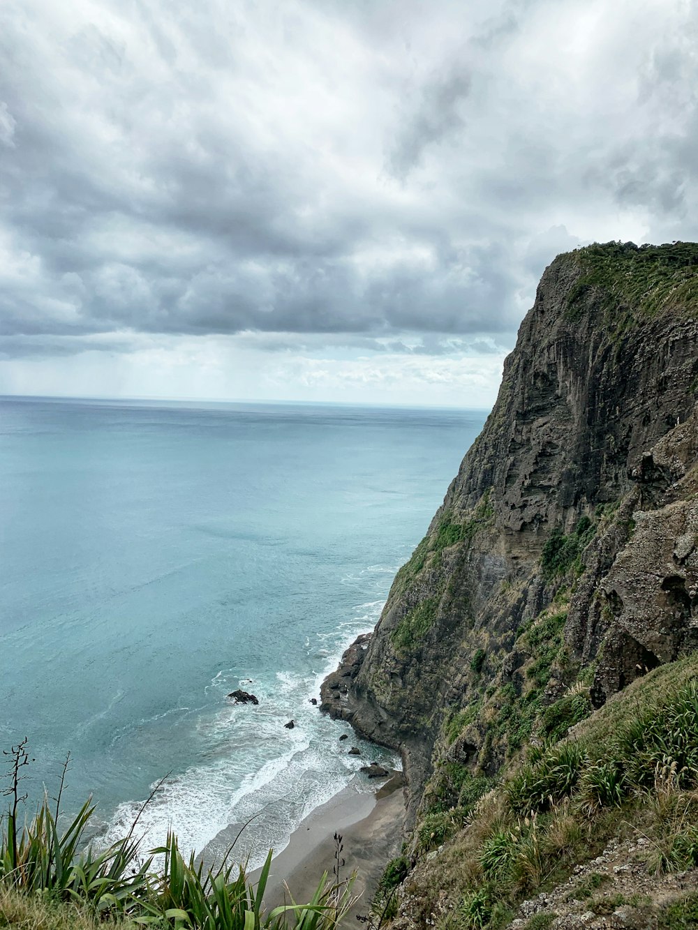 brown and green rock formation beside body of water under white clouds during daytime