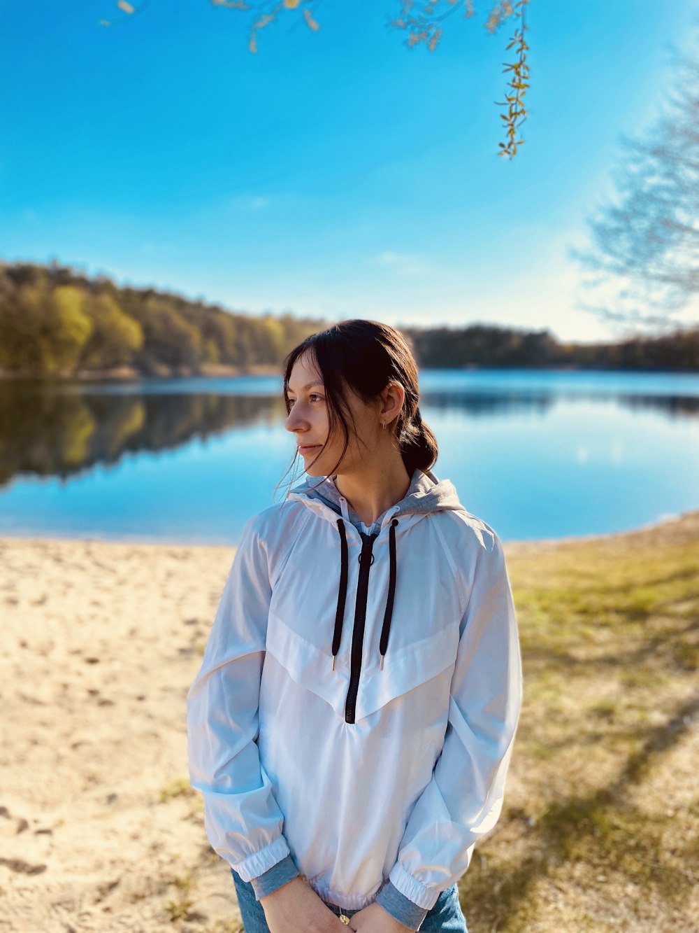 woman in white zip up jacket standing on white sand near body of water during daytime