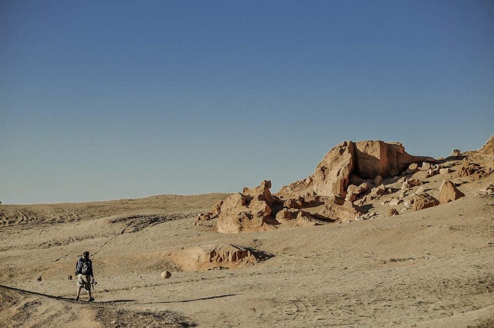 Hombre con chaqueta negra caminando sobre arena marrón durante el día
