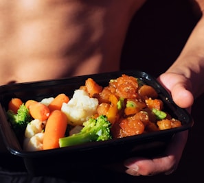 person holding black plastic container with food