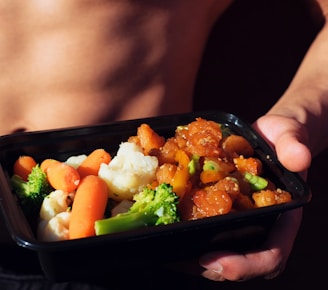 person holding black plastic container with food