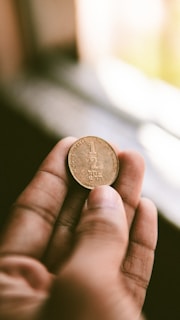 An elegant hand holding a gold coin against a blurred background.