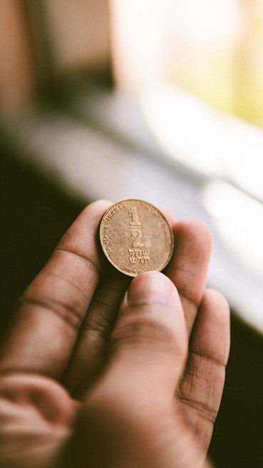 An elegant hand holding a gold coin against a blurred background.