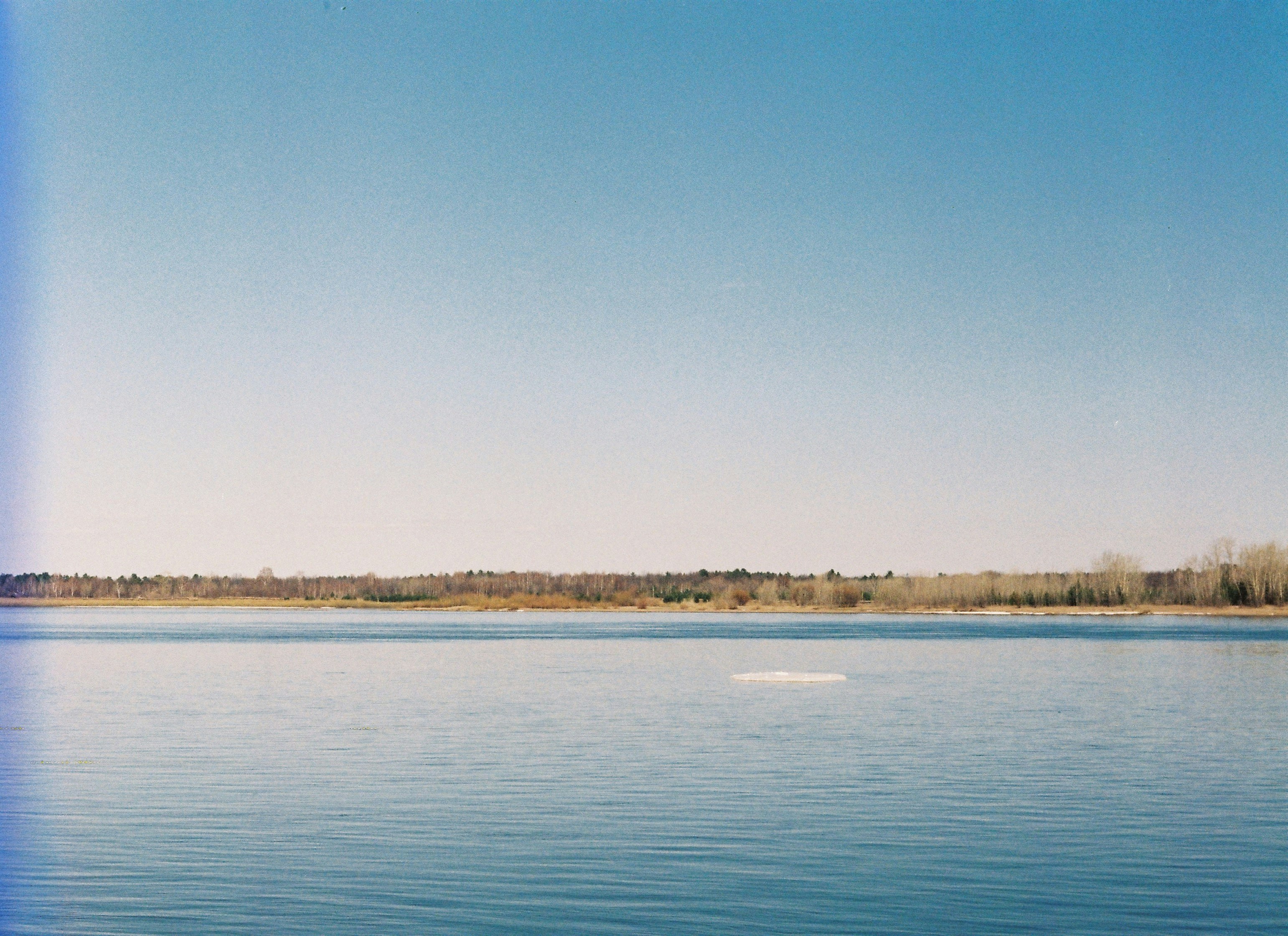 A wide river with an island in the middle, blue sky, blue water. Early spring, sunny day. Minimalism, Perfectionist Paradise. @art.ilya - Сamera roll Kodak.