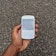 A hand holding a white smartphone with a QWERTY keyboard. The screen displays static or noise, echoing the gravel-like texture in the background.
