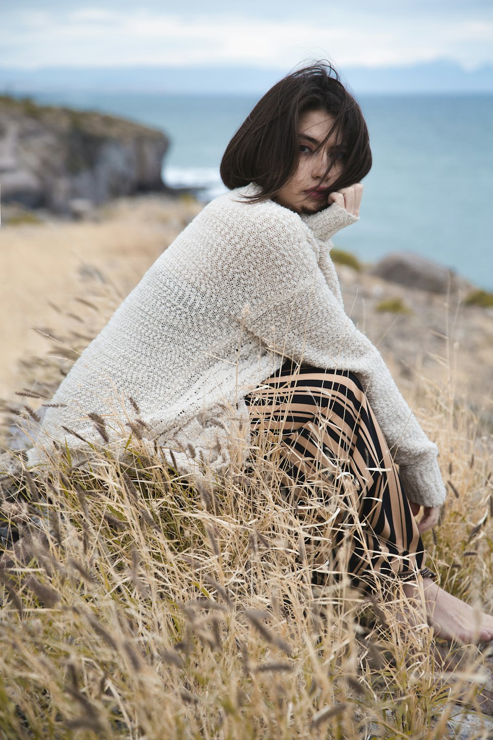 woman in white knit sweater sitting on brown grass field during daytime