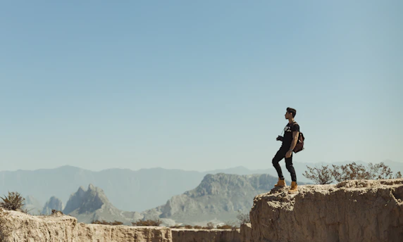 A candid shot of a traveler standing on a rugged cliff, gazing out over a misty valley at dawn, with a vintage compass resting in their hand.