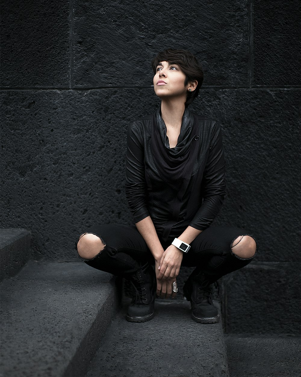 woman in black long sleeve shirt and black pants sitting on gray concrete floor