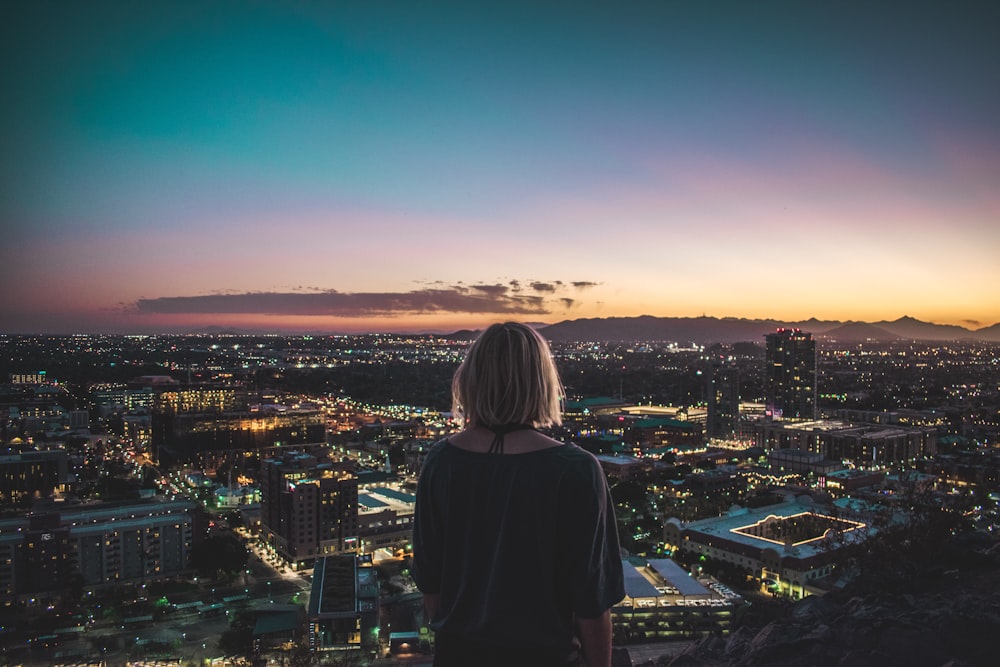 woman in black shirt standing on top of building looking at city lights during night time