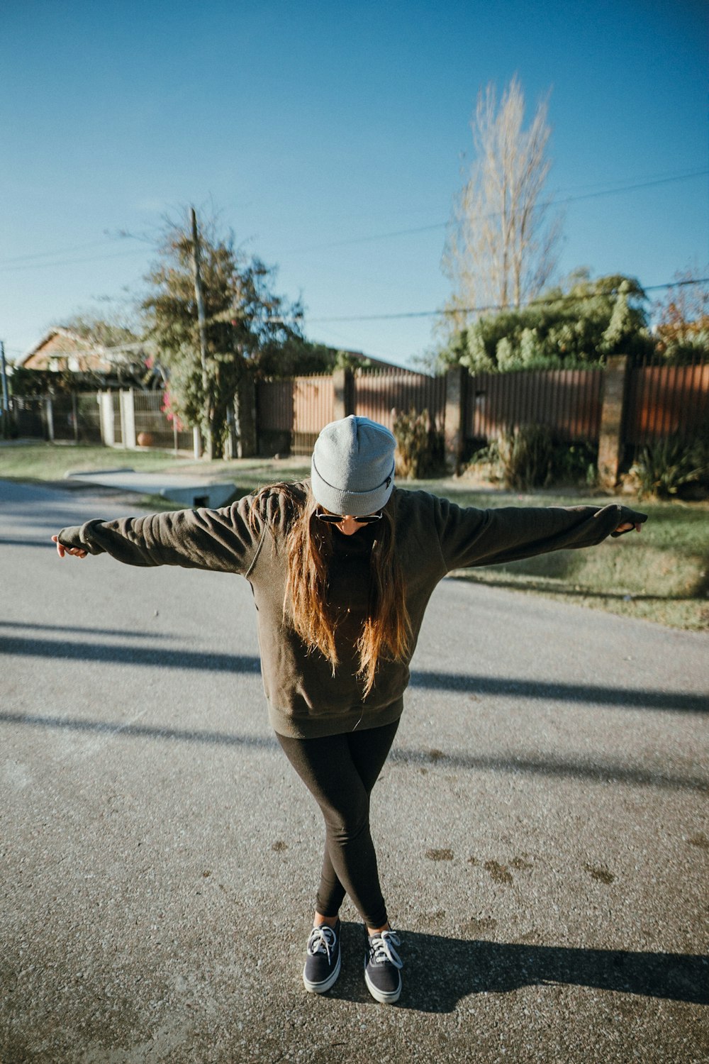 woman in brown jacket and black pants standing on gray asphalt road during daytime