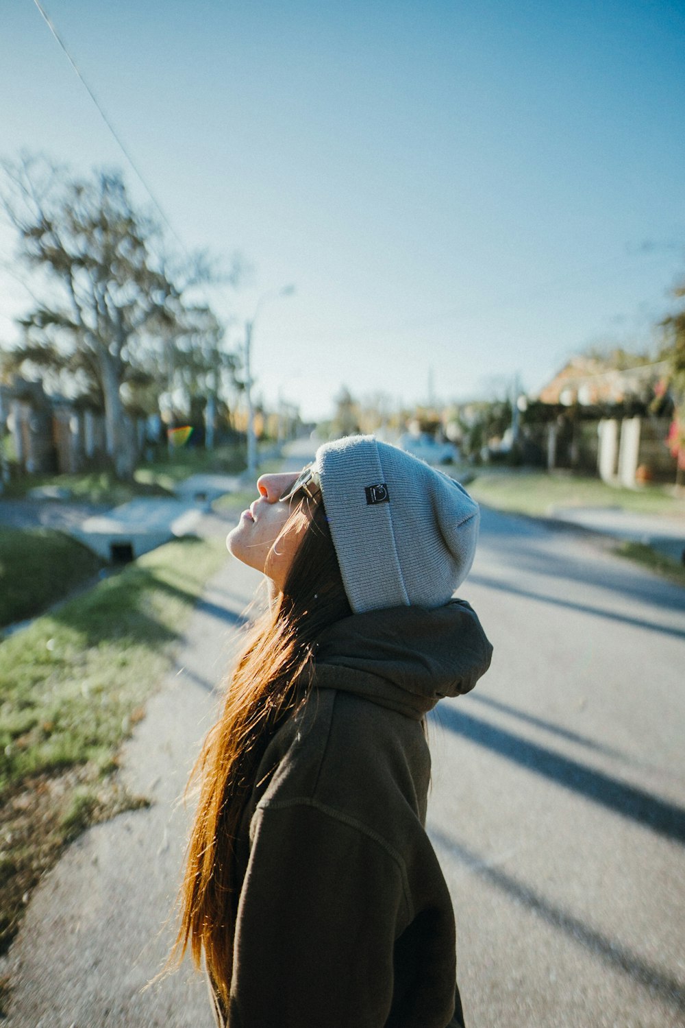 woman in blue knit cap and brown jacket standing on road during daytime