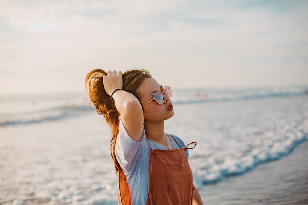 woman in blue shirt wearing sunglasses standing on beach during daytime