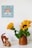 A small wooden toy car and an abstract wooden cat figurine sit on a white surface beside a brown vase containing vibrant sunflowers. A wall sign above features a colorful rainbow and the words 'My Playroom' surrounded by clouds.