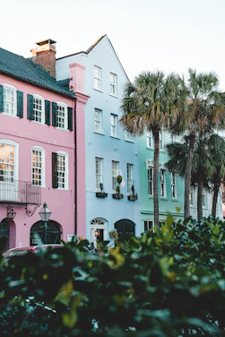 A sun-drenched coastal street lined with lush palm trees and pastel colonial buildings under a vibrant fuchsia sky.