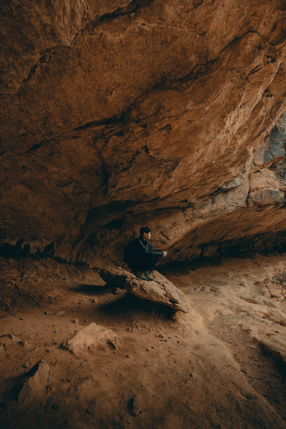 man in black jacket sitting on rock formation during daytime