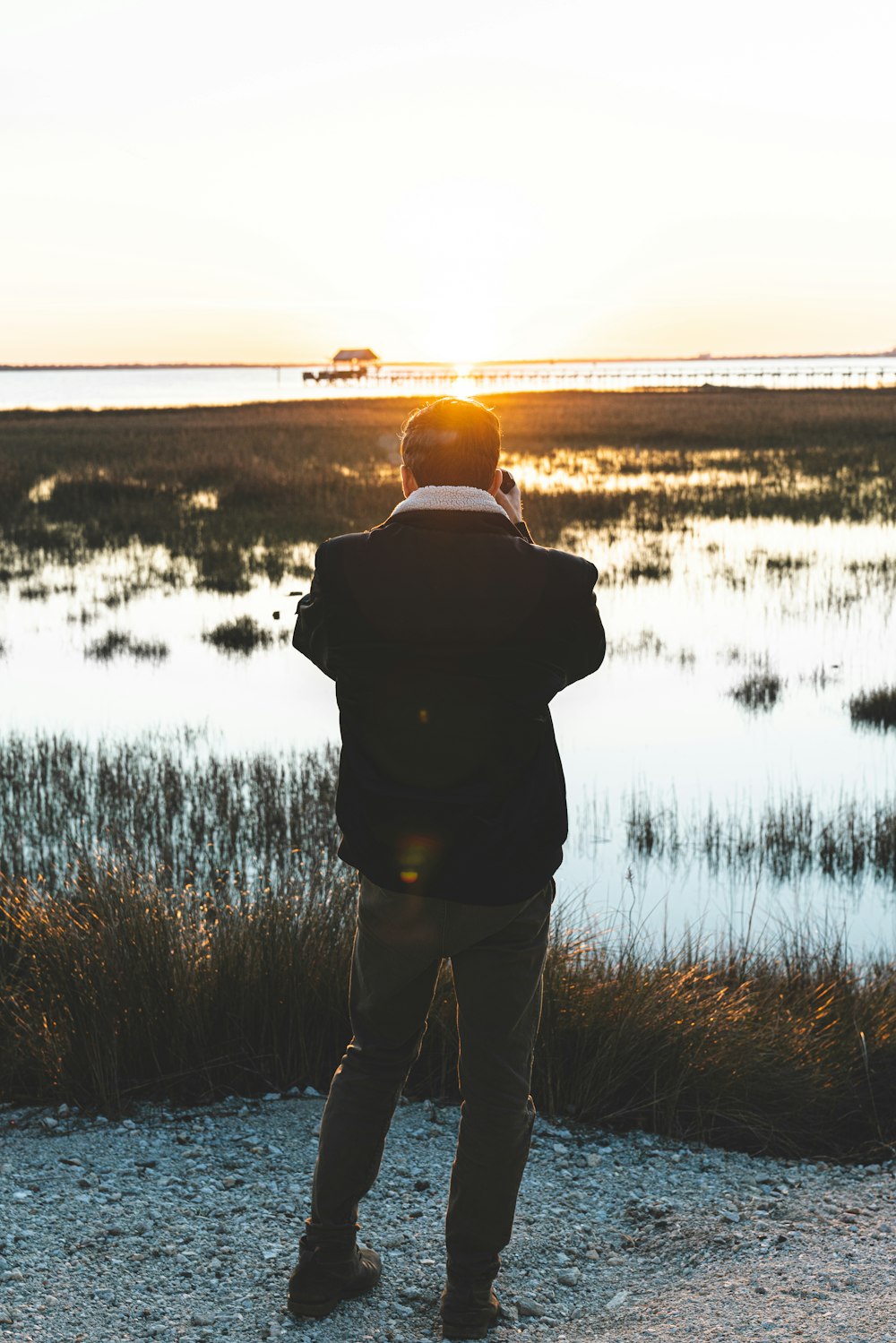 man in black jacket standing on grass field near lake during daytime