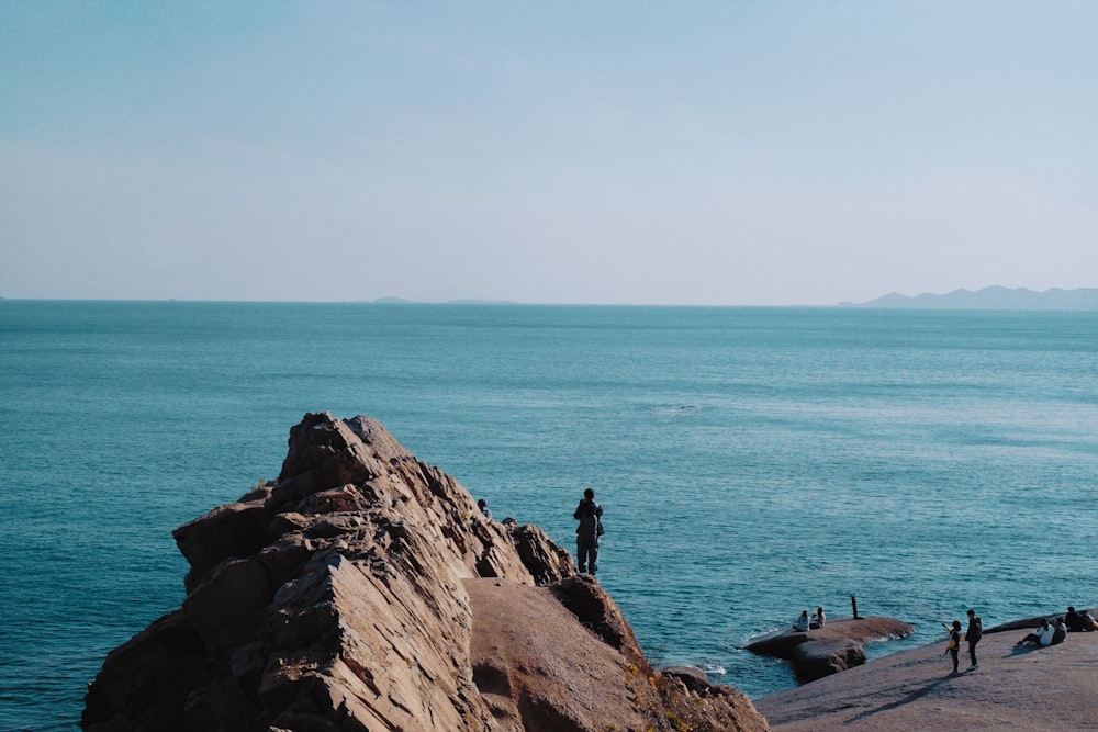 people standing on brown rock formation near body of water during daytime