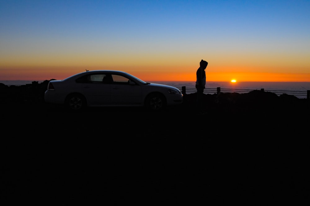 silhouette dell'uomo in piedi accanto alla berlina nera durante il tramonto