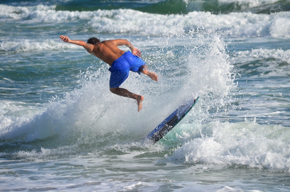 man in blue shorts surfing on sea waves during daytime