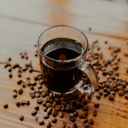 A warm, hand-thrown stoneware mug with earthy glaze sitting on a wooden table next to fresh coffee beans.
