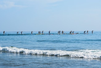 Group of people paddling a Hawaiian canoe on calm ocean waters near a beach.