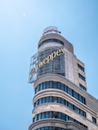 A curved building with a large Schweppes advertisement on the side. The structure is topped with additional signage for Capitol and Vodafone, set against a clear blue sky.