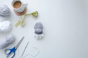 A flat lay of crochet tools including stitch markers, scissors, and a project bag styled with soft shadows.