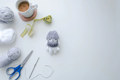 A flat lay of crochet tools including stitch markers, scissors, and a project bag styled with soft shadows.
