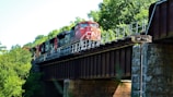 A sleek train passing through a scenic bridge surrounded by lush greenery.