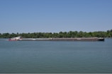 Cargo barge navigating a calm river at sunrise with lush green banks.