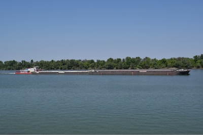 Cargo barge navigating a calm river at sunrise with lush green banks.