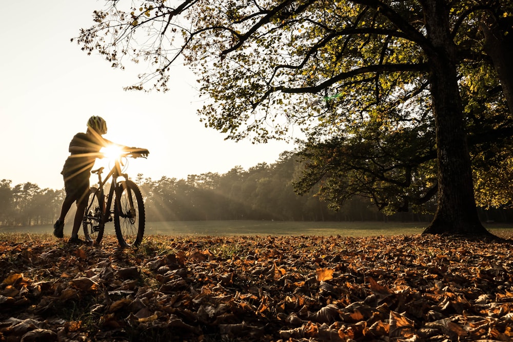 woman in black jacket riding bicycle on brown dried leaves during daytime