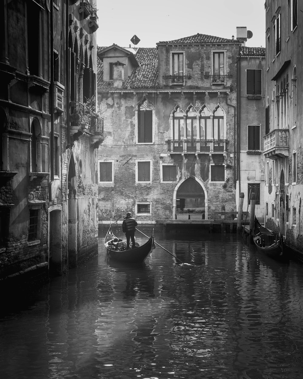 grayscale photo of boat on river between buildings