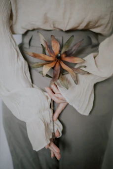 an intimate close-up of hands holding a delicate dried flower on a neutral textured fabric