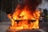 A car engulfed in intense flames on the side of a road with thick black smoke billowing into the air. Firefighters and a fire truck are visible in the background, indicating an emergency response situation.