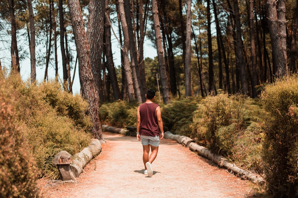 man in red shirt walking on pathway surrounded by trees during daytime