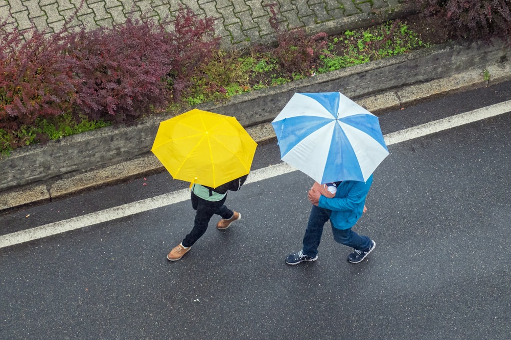 Person in blauen Jeans mit gelbem Regenschirm geht tagsüber auf dem Bürgersteig