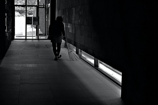 A janitor vacuuming a bright, tidy office corridor with natural light.
