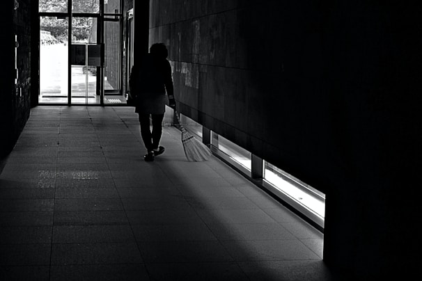 Janitor emptying trash bins in a well-lit hallway.