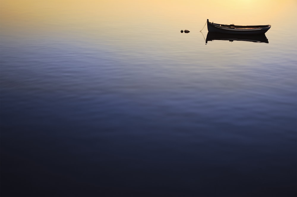 silhouette of boat on calm water during sunset