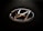 A chrome Hyundai logo with a sleek, rounded design is set against a textured black background, typically found on a steering wheel or vehicle interior.